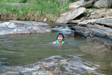 Little girls enjoy swimming in the river. Cute Asian girl wearing a life jacket is having fun playing in the stream. Healthy Summer Activities for Kids.