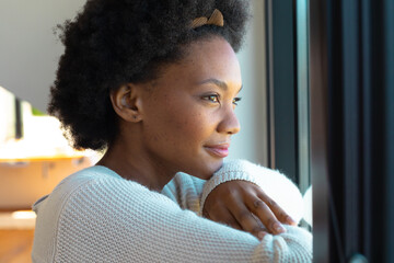 Side view of thoughtful young african american afro woman looking through window at home