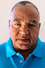 Close-up portrait of biracial senior man with gray eyes against wall in retirement home