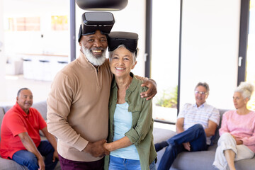 Portrait of happy multiracial senior friends wearing virtual reality simulators in retirement home