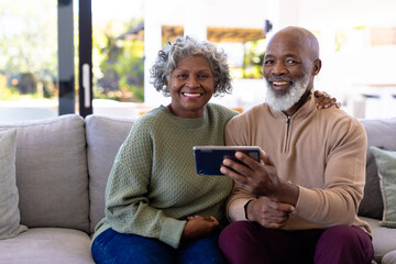 Portrait of smiling african american senior friends with digital pc sitting on sofa in nursing home