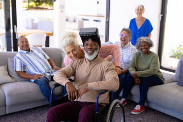 Fototapeta na wymiar Portrait of happy multiracial seniors with man wearing virtual reality sitting on wheelchair