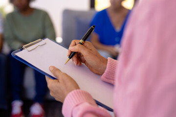 Midsection of caucasian senior female therapist writing on paper with clipboard in nursing home