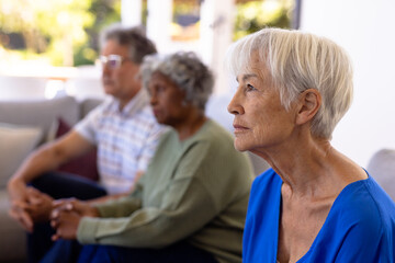 Asian sad senior woman with multiracial friends sitting on sofa in nursing home