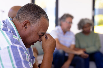 Close-up of depressed caucasian senior man with head in hand sitting with multiracial friends