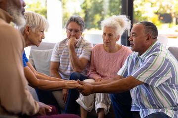 Multiracial seniors holding hands and comforting while sitting with friends in group therapy session