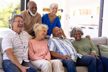Cheerful multiracial male and female senior friends laughing while relaxing in nursing home - obrazy, fototapety, plakaty
