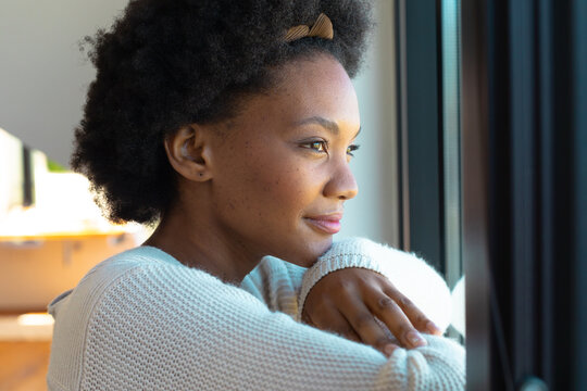 Side view of thoughtful young african american afro woman looking through window at home