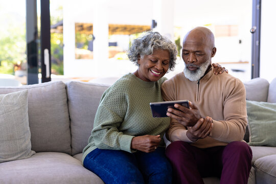 African american senior man with woman watching video over digital tablet on sofa in nursing home