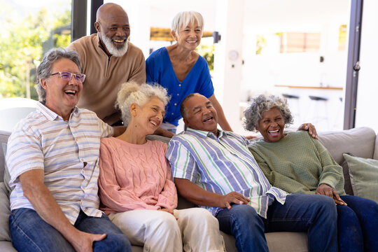 Cheerful multiracial male and female senior friends laughing while relaxing in nursing home