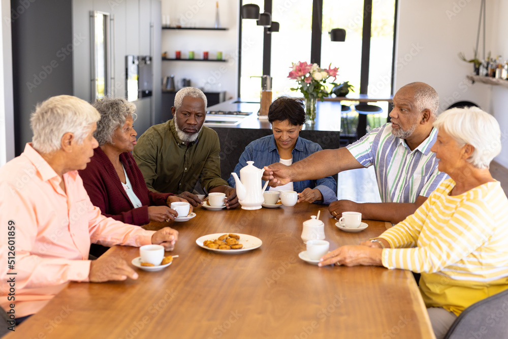 Wall mural multiracial senior friends having coffee and cookies while sitting at dining table in nursing home