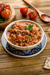 chili con carne with tomatoes and herbs on a wooden table, next to a spoon and vegetables