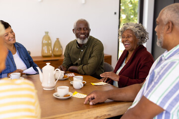 Multiracial cheerful senior friends with bingo, coffee and cookies on dining table in nursing home