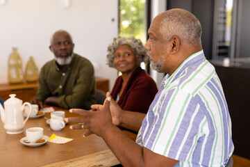 Multiracial senior man talking with friends while having coffee and cookies at dining table