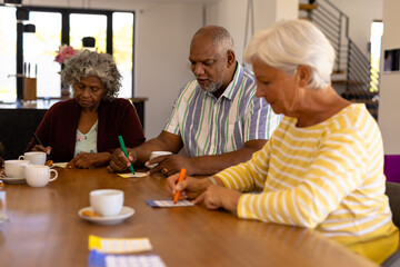 Multiracial senior friends with coffee cups on dining table playing bingo in nursing home