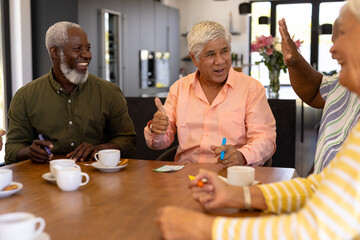 Multiracial happy senior man showing thumbs up while playing bingo with friends at dining table