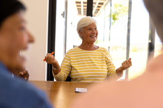 Cheerful Biracial Senior Woman Gesturing While Playing Bingo At Dining Table In Nursing Home