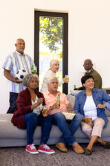Multiracial senior friends enjoying beer and popcorns while watching soccer match in nursing home