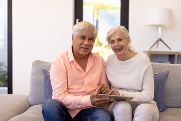 Portrait of cheerful multiracial senior friends with digital tablet sitting on sofa in nursing home