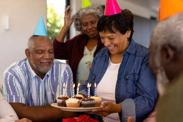 Happy multiracial senior woman holding cupcakes with candles while enjoying birthday with friends