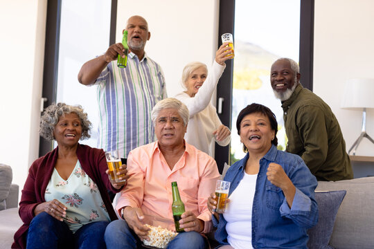 Multiracial excited senior friends with beer and popcorns enjoying match in nursing home