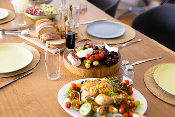 High angle view of chicken with cherry tomatoes, cheese, bread and grapes served on dining table