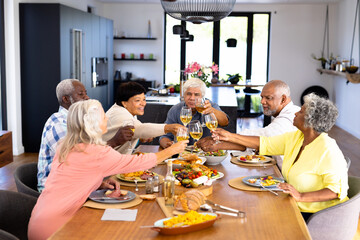 Happy multiracial senior friends toasting wineglasses while having lunch at dining table