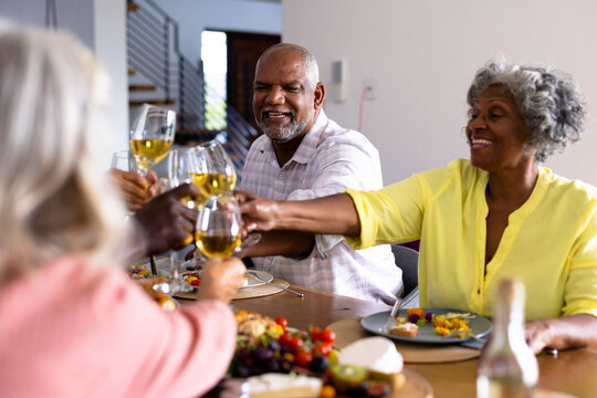 Multiracial cheerful senior friends toasting wineglasses while having lunch at dining table