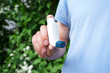 Male hand holding asthma inhaler on attack outdoor, close-up. Health and medical concept.