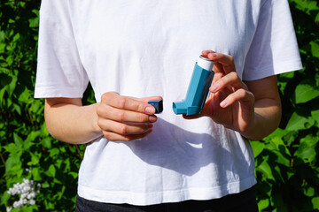 Hands of a young woman holding a blue asthma inhaler outdoors. Pharmaceutical drug for the relief...