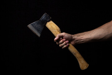 A man's hand holds an ax on a black background. Small old ax
