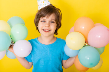 Handsome Little birthday boy in blue shirt and hat with balloons, yellow background, happy birthday