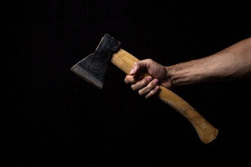 A man's hand holds an ax on a black background. Small old ax