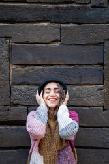 Mujer sonriente con gorro parada frente a la cabaña sujetándose el sombrero - obrazy, fototapety, plakaty