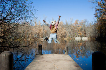 Mujer saltando de felicidad en el embarcadero de un lago en mitad del bosque. Mujer feliz
