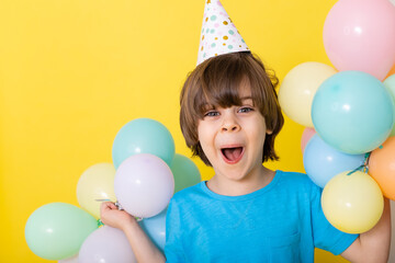 Handsome Little birthday boy in blue shirt and hat with balloons, yellow background, happy birthday