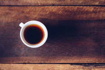 A shot glass of black coffee on wooden table.