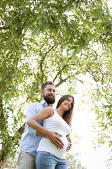 Fototapeta premium pretty young pregnant woman with white shirt stands with her boyfriend with beard and blue shirt in high flower meadow and cuddle