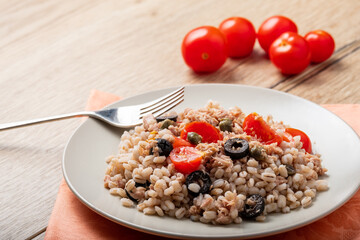 salad of pearl barley, tuna, cherry tomatoes and olives, on a white plate with fork