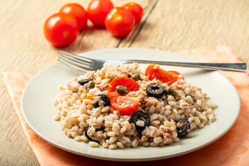 salad of pearl barley, tuna, cherry tomatoes and olives, on a white plate with fork