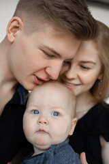 Portrait of young good-looking family in dark clothes with plump cherubic baby infant toddler kiss on white background.