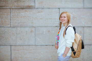 happy trendy pupil in sweatshirt against wall outdoors in city