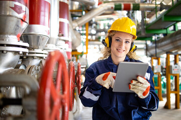 Portrait of heating plant female worker standing by valves and pipes checking water temperature on...