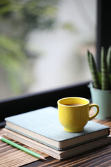 Notebook and yellow cup on and plant pot wooden table in fornt of window