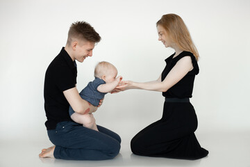 Portrait of young beautiful family in dark clothes with plump cherubic baby infant toddler sitting on white background.