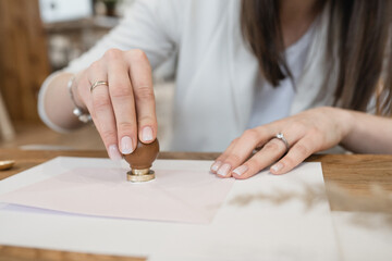 Well-groomed hands with rings of unrecognizable woman making wax seal with stamp on white envelope...