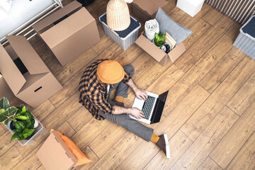 Hipster man with moving boxes in new modern apartment. Happy mature man sitting on the floor of a newly rented ore purchased apartment using a laptop. Unpacked cardboard boxes and furniture in a