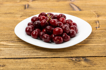 ripe red cherries in a white plate on a wooden background