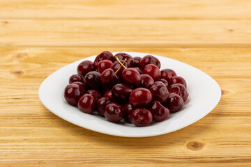 ripe red cherries in a white plate on a wooden background