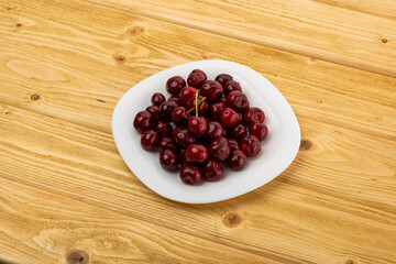 ripe red cherries in a white plate on a wooden background
